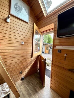 Interior de una cabaña de madera con ventana, puerta y televisor montado.