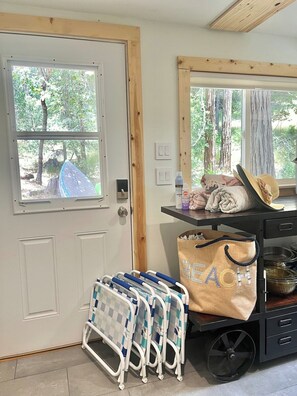 Una habitación con puerta, ventanas, un carrito con maletas y vista a árboles.