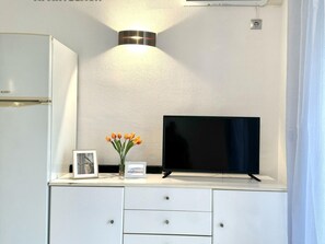 A white minibar with a flat-screen TV, a framed photo, and a vase of tulips. - Seaside loft in Salou with AC and terrace (Salou)