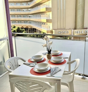 A dining table set with white plates and red placemats on a balcony with a view of a hotel building. - Seaside loft in Salou with AC and terrace (Salou)