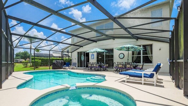 Una piscina exterior techada con sillas de descanso y sombrillas, rodeada por una casa.