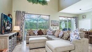 Amplia sala de estar con sofá modular, otomanas, televisor y comedor.