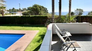 A swimming pool with a wooden deck, a seating area with chairs, and a view of the sea. - Beautiful beachfront apartment with pool and private parking (Miami Playa)