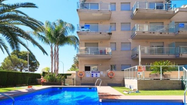 A swimming pool with a wooden deck, surrounded by a high-rise building with balconies. - Beautiful beachfront apartment with pool and private parking (Miami Playa)