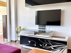 Una sala de estar moderna con un televisor de pantalla plana montado en la pared, un mueble de entretenimiento elegante debajo y una mesa de centro de vidrio.