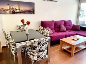 Una sala de estar moderna con una mesa de comedor, un sofá púrpura y un cuadro de un puente.