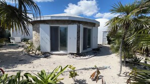A small, white, single-story building with a curved roof, surrounded by sand and tropical vegetation. - On the beach, Private path to the ocean beach. (Cat Island)