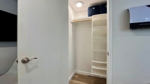 Een inloopkast met een witte deur, een luchtverfrisser aan het plafond en een houten vloer.