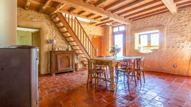 A rustic kitchen with a wooden staircase, a dining table with chairs, and a refrigerator. - RURAL ECOGITE LA CLE DES CHAMPS (Peyrelongue-Abos)