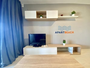 Una sala de estar moderna con un televisor de pantalla plana, una mesa de centro de madera y un estante fijado a la pared con plantas en macetas.