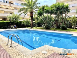 A swimming pool with a ladder, surrounded by palm trees and greenery, with a building in the background. - Beautiful 2-bedroom apartment with pool, near the beach in La Pineda (La Pineda)