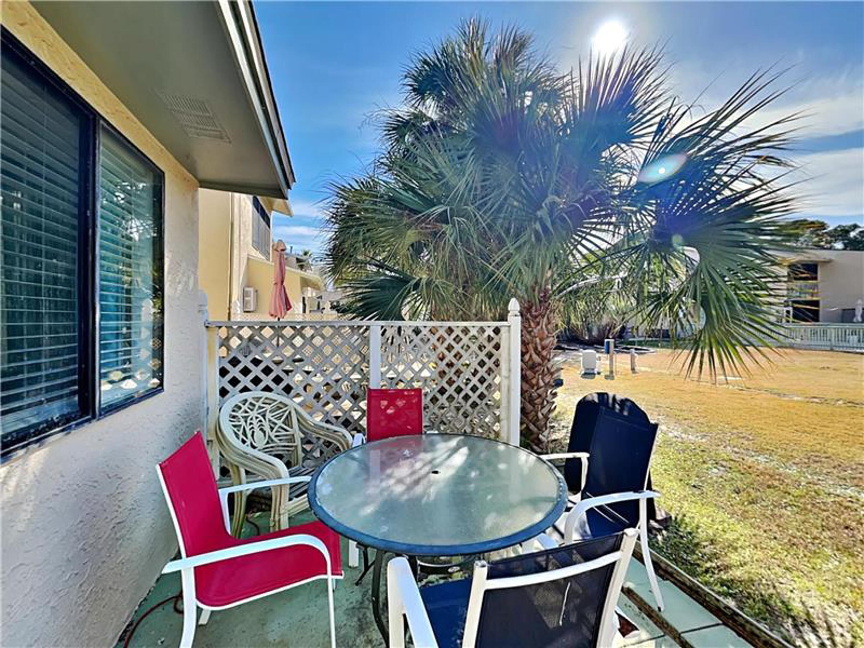 A patio with a round glass table and chairs, a palm tree, and a white lattice fence.