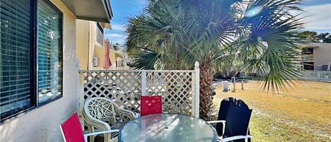 A patio with a round glass table and chairs, a palm tree, and a white lattice fence.