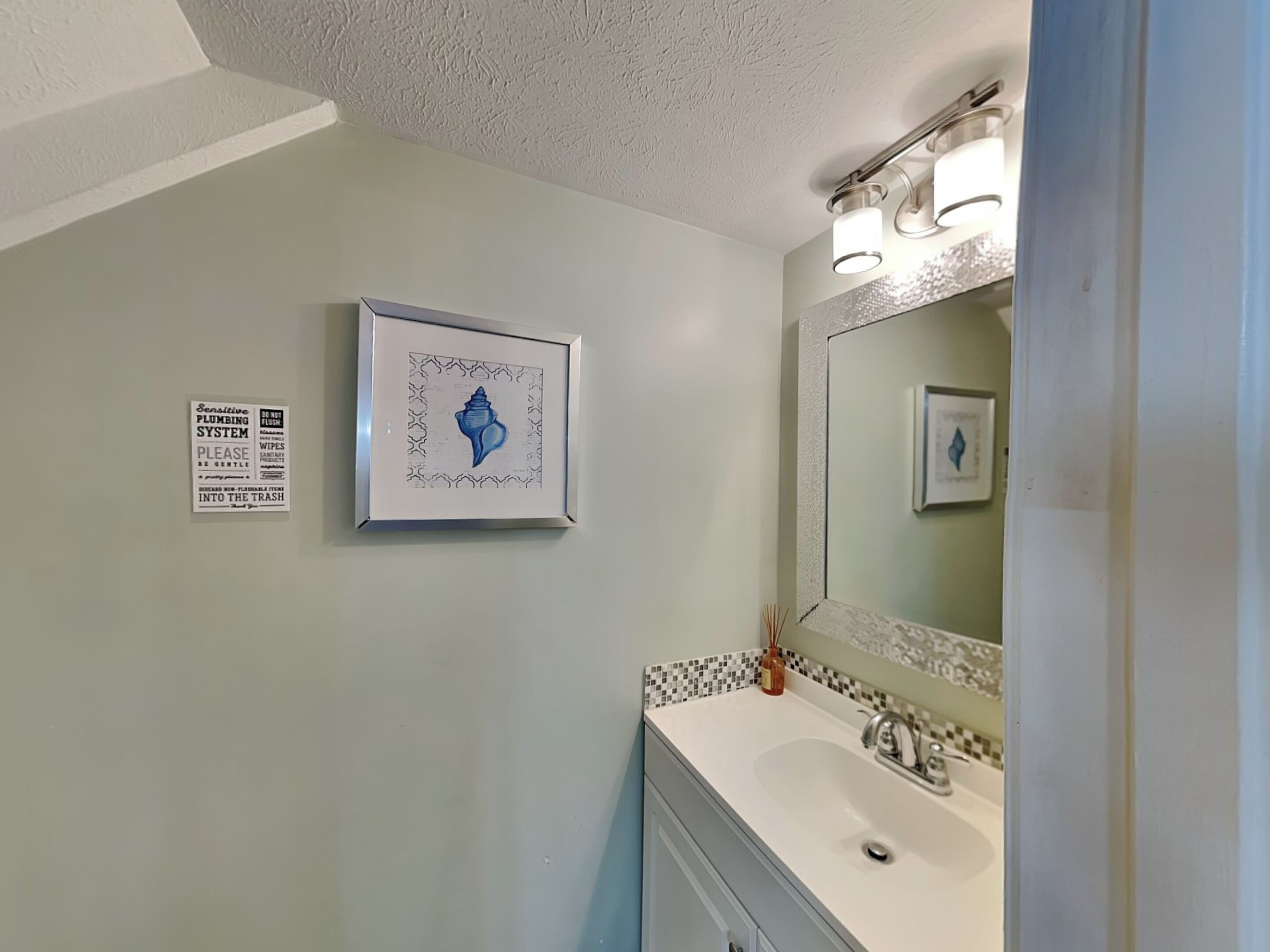 A bathroom with a sink, mirror, and a framed artwork on the wall.
