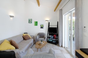 A modern living room with a sofa, armchair, coffee table, and a sliding glass door leading to an outdoor area. - Villa in Residence with Pool Near Porto-Vecchio for 6 Guests (San-Gavino-di-Carbini)