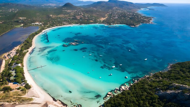 Luftaufnahme einer Küstenregion mit klarem türkisblauem Wasser, einem Sandstrand und verstreuten Booten.