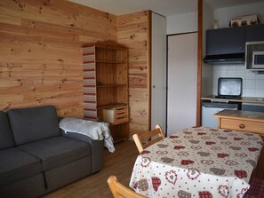 Ein kompakter Raum mit einer Sitzecke, einem kleinen Tisch, einer Tischdecke mit Muster, einem Fernseher und einer Küchenzeile mit Mikrowelle und Herd.