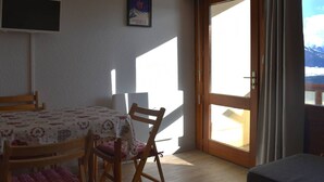Ein Zimmer mit Esstisch, Stühlen, einem an der Wand montierten Fernseher, einem gerahmten Bild und einer Schiebetür zu einem Außenbereich.