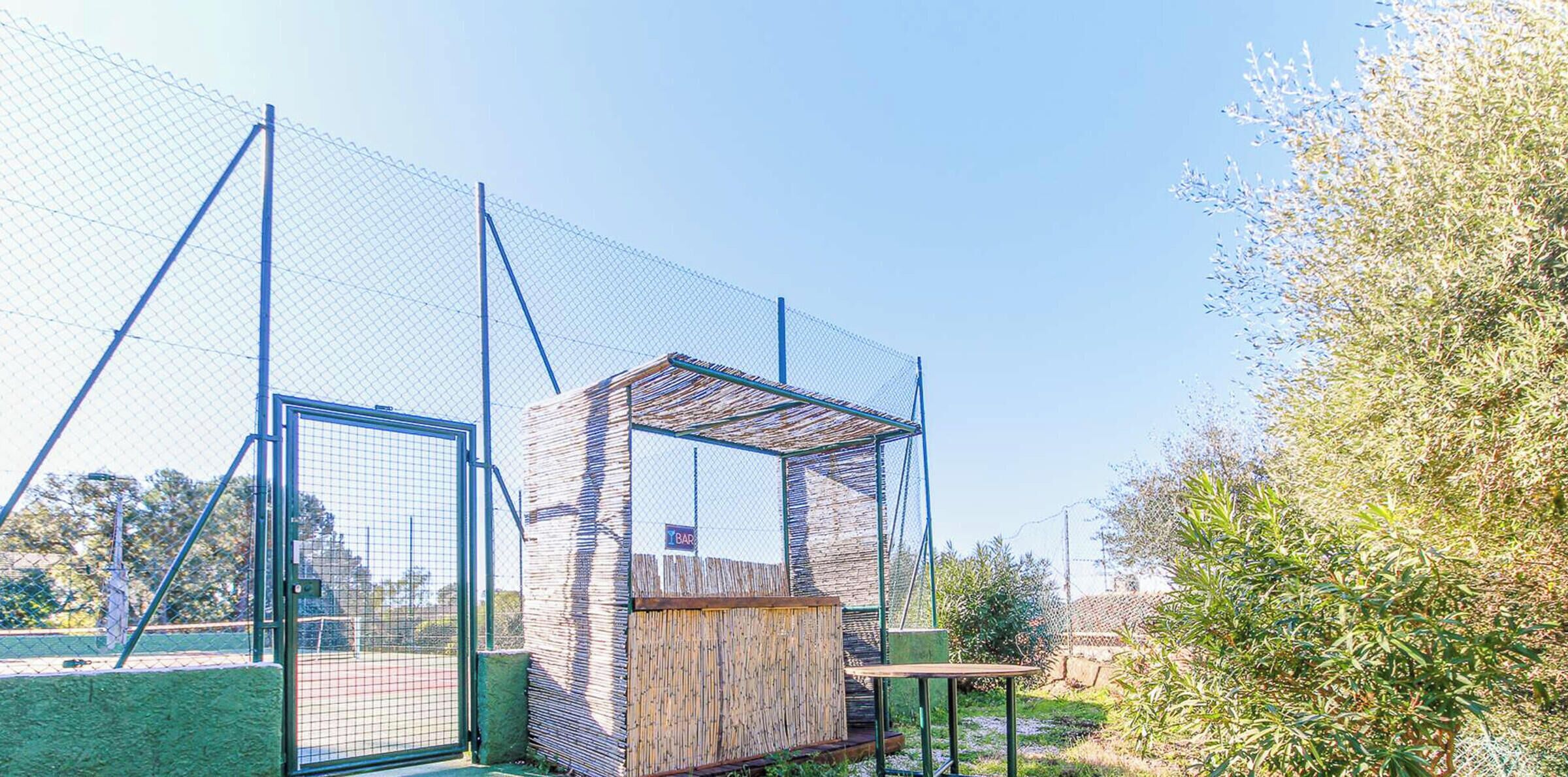 A fenced sports area with a small wooden structure, possibly a changing room or storage, and a sign indicating a bar.