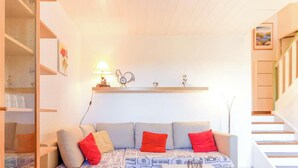 A cozy room with a sofa, a lamp, a clock, and a shelf with decorative items. - Provençal Mazet with Pool, Pets Welcome, Secure Parking (Le Lavandou)