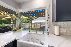 A kitchen with a built-in sink, a window overlooking a backyard, and a herringbone-patterned backsplash. - South ATX Home Sauna, Parking, Cowboy Pool (Austin)