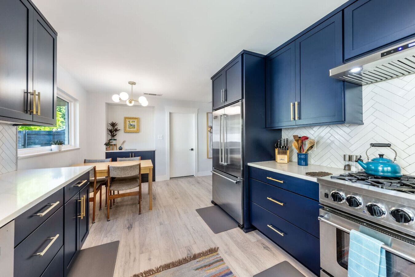 Une cuisine moderne avec des meubles de couleur bleu foncé, des appareils électroménagers en acier inoxydable et une table à manger en bois.