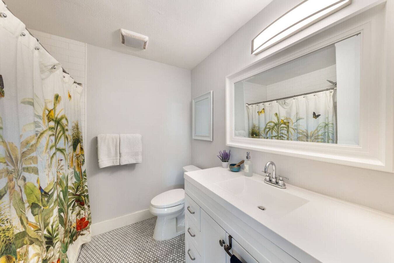 A bathroom with a white toilet, a sink with a mirror above it, and a shower curtain with a tropical print.