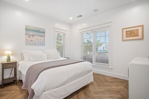 A bedroom with a bed, bedside table, lamp, artwork, and windows. - Beachfront Haven | Grill • Hot Tub • Sunset Views! (South Haven)