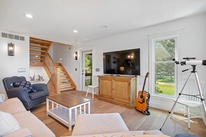 A modern living room with a staircase, a television, a guitar, and a telescope. - Beachfront Haven | Grill • Hot Tub • Sunset Views! (South Haven)