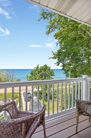 A covered outdoor area with wicker furniture, a white railing, and a view of the ocean. - Beachfront Haven | Grill • Hot Tub • Sunset Views! (South Haven)