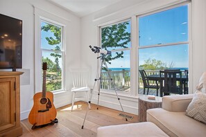 Ein Zimmer mit einer Holzgitarre, einem Teleskop, einem weißen Stuhl und Blick ins Freie durch große Fenster.