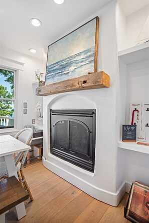 A modern living room with a fireplace, a painting of a seascape, a wooden shelf, and a 'Welcome' sign. - Beachfront Haven | Grill • Hot Tub • Sunset Views! (South Haven)