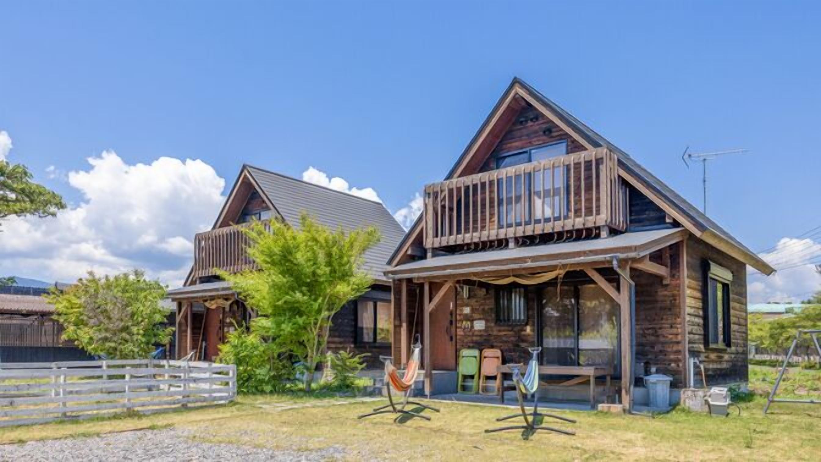 A two-story wooden house with a balcony, a fenced yard, and a hammock.