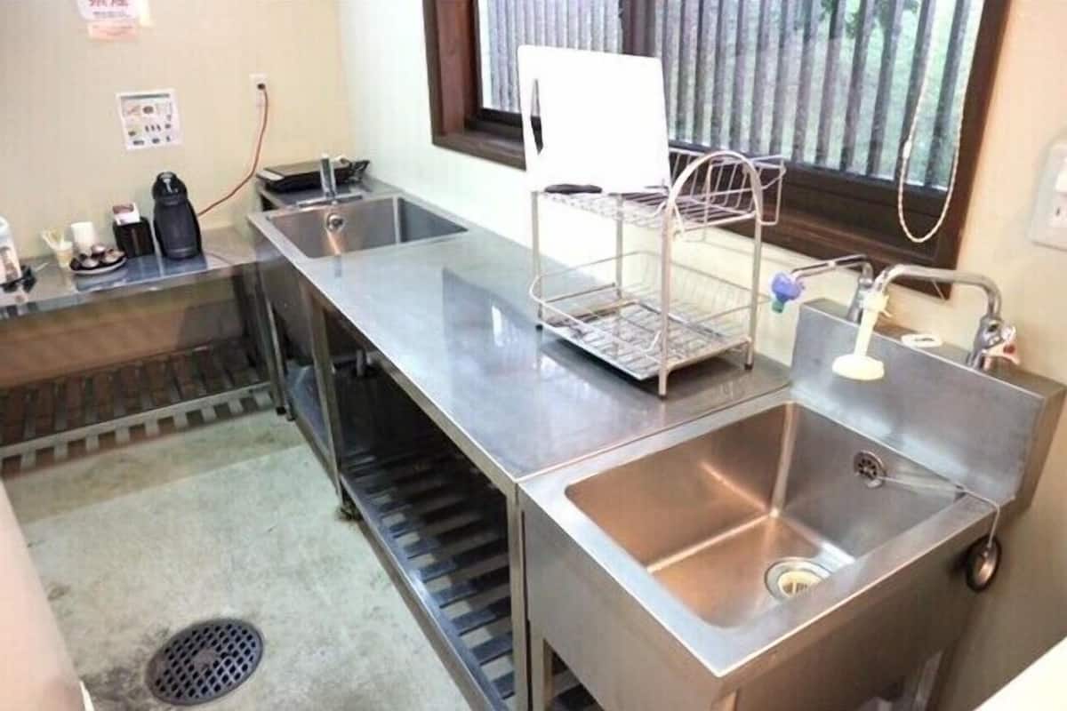 Una cocina con electrodomésticos de acero inoxidable, un lavamanos y un ventanal con persianas.