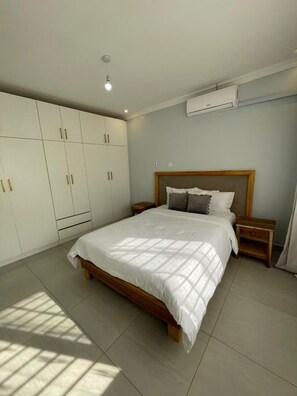 Un dormitorio con cama, mesitas de noche, armario y aire acondicionado.