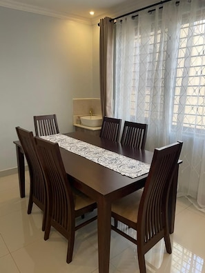 Un comedor con una larga mesa de madera, seis sillas y un camino de mesa estampado.