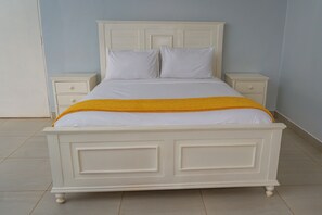Un lit blanc avec une couverture jaune, deux tables de chevet et une commode blanche.