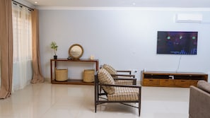 A living room with a sofa, a TV, a wooden console table, and a floor lamp. - Large spacious family friendly 4 bedroom home in Lilongwe (Lilongwe)