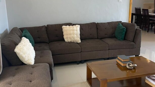 A living room with a sectional sofa, a matching ottoman, a wooden coffee table, and two wall-mounted abstract art pieces. - Large spacious family friendly 4 bedroom home in Lilongwe (Lilongwe)