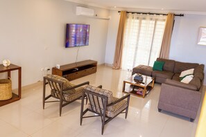 Una sala de estar con un sofá, dos sillones estampados, una mesa de centro, un televisor y una ventana con cortinas.