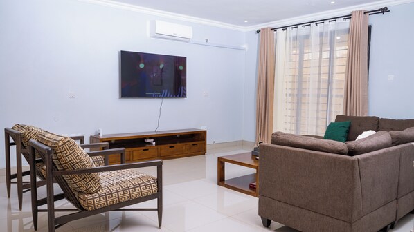 A living room with a sofa, a chair, a coffee table, and a TV mounted on the wall.