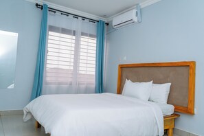 Un dormitorio con una cama, cabecero de madera, ventana con cortinas y un equipo de aire acondicionado.