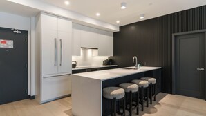 A modern kitchen with a central island, bar stools, and a dark accent wall. - Veldt Haus (Revelstoke)
