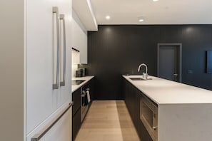 A modern kitchen with a dark wood panel wall, a white countertop, and stainless steel appliances. - Veldt Haus (Revelstoke)