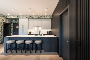 A modern kitchen with a central island, bar stools, and a patterned backsplash. - Veldt Haus (Revelstoke)