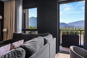 A modern living room with a grey sofa, a large window, and a view of mountains. - Veldt Haus (Revelstoke)