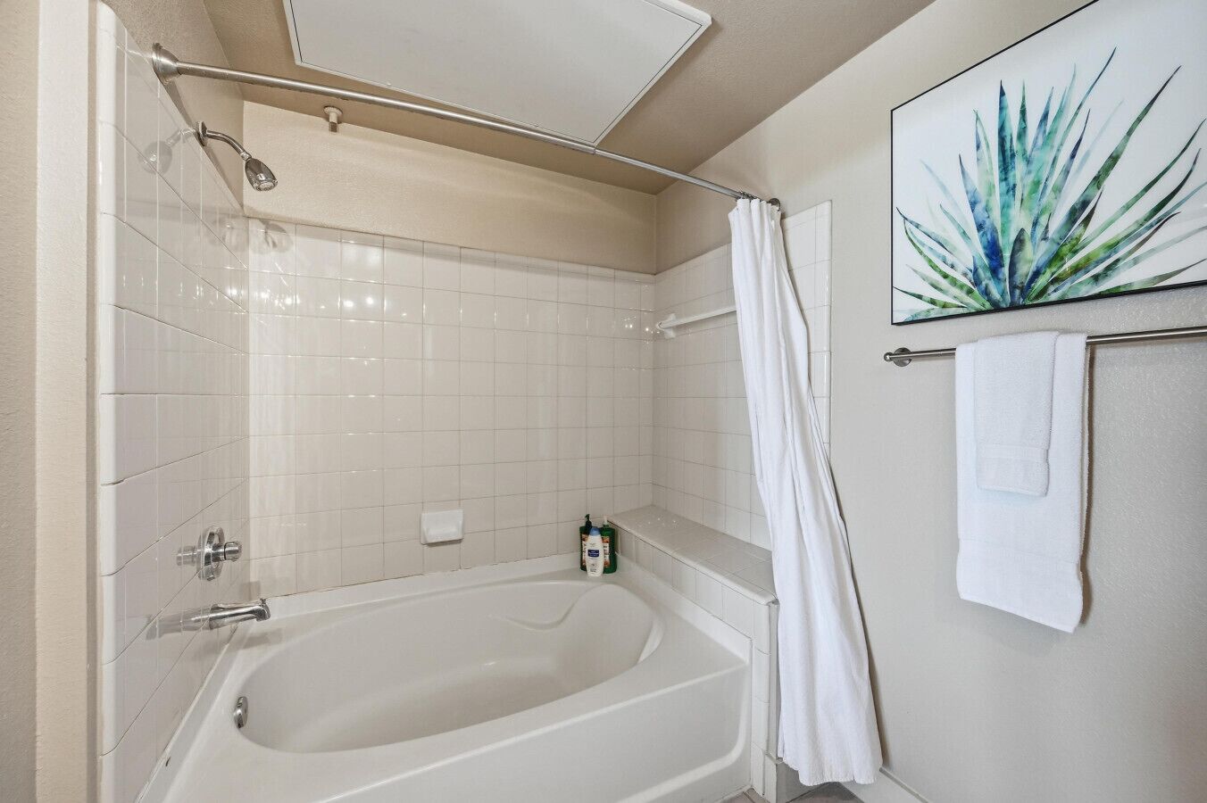 A bathroom with a bathtub, a shower, white tiles, a towel rack with a towel, and a framed picture on the wall.