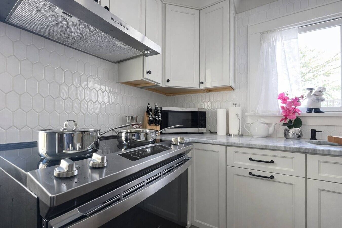 Una cocina moderna con armarios blancos, una estufa de acero inoxidable y un microondas.