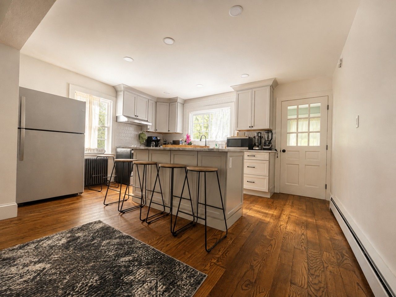 A modern kitchen with a central island, bar stools, a refrigerator, and a microwave.