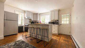 A modern kitchen with a central island, bar stools, a refrigerator, and a microwave.